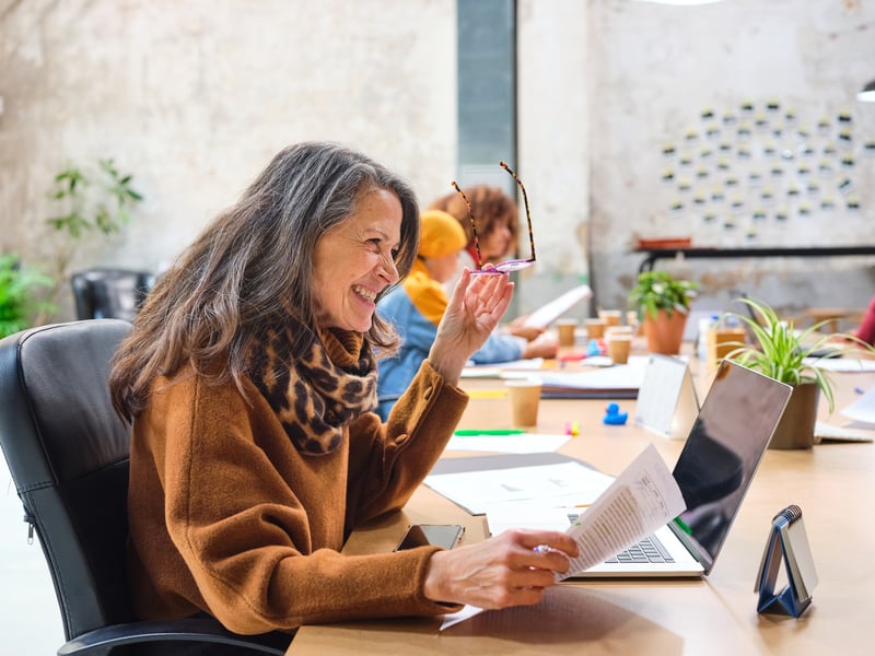 businesswoman-in-40s-working-in-common-working-space-with-document-holding-eyeglasses-and-smiling-taking-initiative
